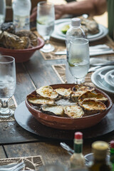 Grilled oysters with melted cheese served on coarse salt in a rustic clay dish at table