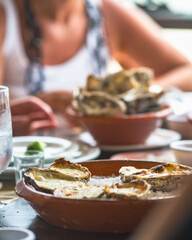 Grilled oysters with melted cheese served on coarse salt in a rustic clay dish at table