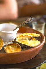 Grilled oysters with melted cheese served on coarse salt in a rustic clay dish at table