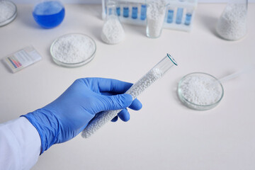 A lab worker holding white thermoplastic beads out of a glass flask.