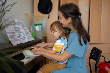 Mother and child playing piano together at home while pet parrot sits on keys.
