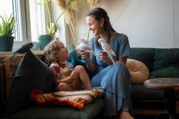 Happy mother and child sitting on a sofa while bonding with parrots indoors  © Dexon Dee