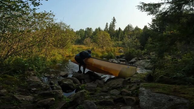 Cinematic 4K view of a Hispanic man lifting his canoe at the start of a portage in Temagami, Ontario