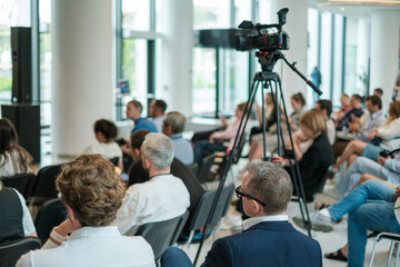 Business seminar with engaged audience in modern bright venue, with professional camera setup.