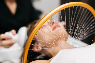 Asian woman receiving hydromassage head treatment at a Japanese spa, with water jets providing...