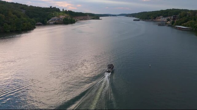 aerial flyover of a lake flanked by trees and docks tilting up to the skyline while a boat passes by