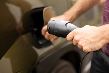 Extreme close up of man closing vehicle inlet port of EV automobile after resupplying with...