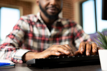 Closeup view of black male hands typing business data for project management. African american remote worker seated at desk, inputting financial information on desktop pc for corporate planning.