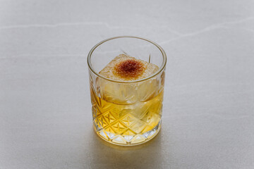 Elegant whiskey cocktail with ice cube and aromatic garnish in a crystal glass on gray stone