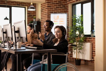 Smiling female employee, wearing wired headphones, works diligently at her desk. Caucasian woman in...