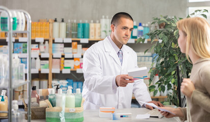 While working with girl client, man pharmacist reads instructions for drug on computer, checks...