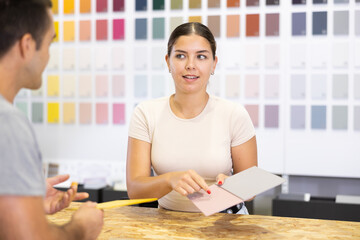 Female saleswoman of paintwork material department stand with samples of product and catalog at...