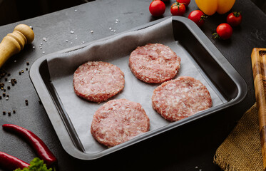 Fresh raw burger cutlets with spices and vegetables on black background, ready for cooking