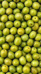 A close-up view of many vibrant green olives, densely packed together, showcasing their glossy, smooth surfaces and tiny pits.