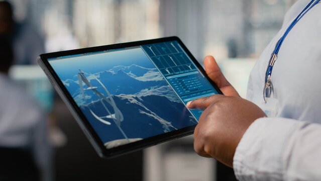 Close up of engineer working on futuristic vertical wind turbine CAD design used for green energy research. Worker using digital modeling tablet app to upgrade wind VAWT energy generator gear