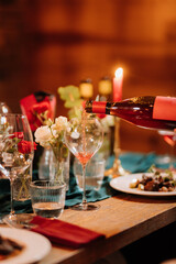 Pouring rose wine into glass at festive dinner with flowers and candlelight ambiance