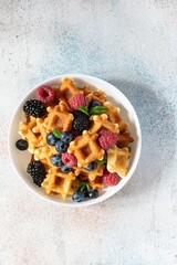 Tiny Mini waffles waffles with berries in a white bowl on a light background. Delicious breakfast