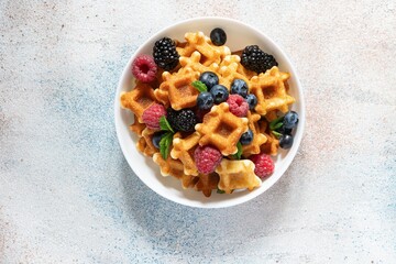 Tiny Mini waffles waffles with berries in a white bowl on a light background. Delicious breakfast