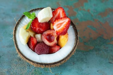 Fruit salad in a bowl of half coconut on a gray background with a place for text, copy space. Healthy natural organic food, low calories delicious dessert. Vegan concept