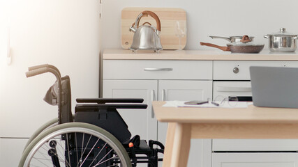 Home recovery after injury, work remotely, new normal. Cheerful mature african american disabled guy stands with crutch in wheelchair, drinking coffee in kitchen interior with laptop, copy space
