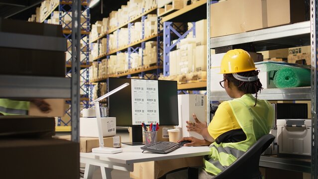 Storehouse black worker reviewing digital shipment status, using awb numbers on tracking software. Woman handling data driven order tracking and delivery updates in warehouse. Camera A.
