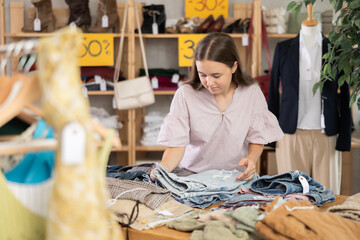 Teenage girl came to the sale in store and chooses jeans and shorts for the summer.