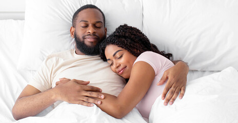 Calm millennial african american female and male sleeping at night, hugging on bed in bedroom...