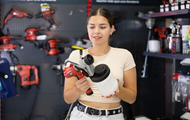 Woman examines handheld wireless portable spray gun, airbrush in tools department of construction...