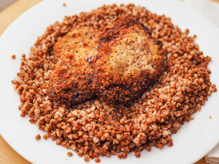 Simple tasty buckwheat and breaded chicken fillet meal on a white round plate.