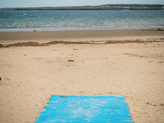 End of a blue wooden walk path on a sandy beach, ocean in the background. Warm summer day.