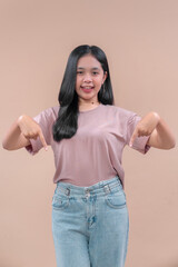 A young Asian woman in a casual modern outfit smiles confidently, pointing down with both hands, expressing cheerful and stylish attitude.