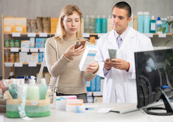 Near display case in pharmacy, girl scans barcode on emollient packaging, reads user manual. Woman...