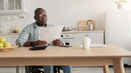 African american freelancer typing on computer, paperwork with documents on table. Smiling mature...