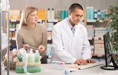 Man pharmacist is working at computer, collaborate with girl client.Electronic database of drugs,...