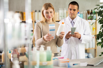 Selective young girl choosing cream while male pharmacist giving offer in chemistry