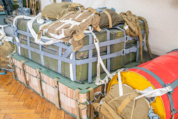 Storage area with stacked wooden crates, strapped cylindrical object, yellow and red tones, parquet floor, artificial lighting