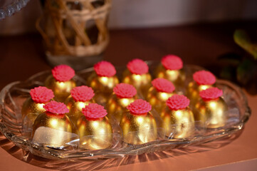 gourmet chocolate truffles with a pink flower topping, luxurious golden sweets for a party, artisanal bonbons on a glass plate, handmade confectionery in festive wrapping, golden chocolates


