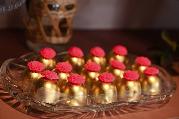 gourmet chocolate truffles with a pink flower topping, luxurious golden sweets for a party, artisanal bonbons on a glass plate, handmade confectionery in festive wrapping, golden chocolates


