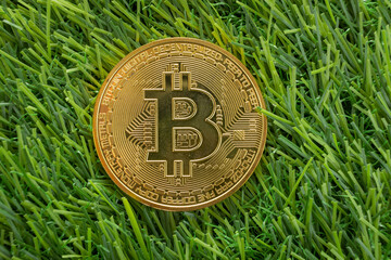 An eye-level shot of a golden Bitcoin coin resting on a patch of vibrant green artificial grass.