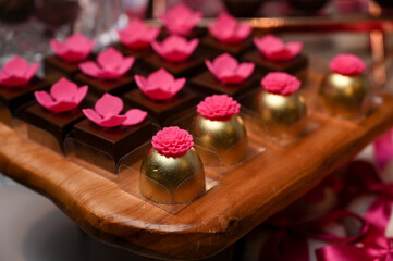 gourmet chocolate truffles and golden sweets, elegant sweets arrangement for a special event, beautiful party desserts with pink flowers, delicious confectionery on a wooden tray

