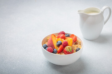 Healthy breakfast with oatmeal porridge with peach, strawberry, raspberry, blueberry and milk in white bowl on gray background, perfect for a nutritious and energizing start to the day, copy space