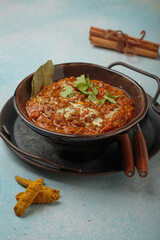 Steaming bowl of Dal makhani, a traditional indian lentil dish, garnished with fresh coriander and cream, presented on a rustic metal tray with turmeric and cinnamon on blue background