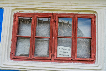 Close-up view of a peeling red, multi-pane window in an ancient Central European building Paper with indistinct writing on one pane, set against white and blue walls Natural lighting, shallow depth