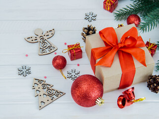 The Christmas tree branch is decorated with toys, a gift box with a red ribbon and wooden toys on a white wooden background
