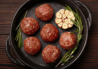 Raw meatballs seasoned with garlic and rosemary ready to be cooked in a cast iron pan, on a dark...