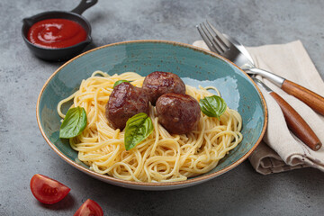 Plate of spaghetti topped with meatballs and basil leaves, accompanied by tomato sauce, fork,...