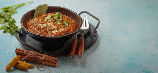 Steaming bowl of Dal makhani, a traditional indian lentil dish, garnished with fresh coriander and cream, presented on a rustic metal tray with turmeric and cinnamon on blue background, copy space