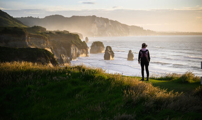 Woman standing on the top of the hill at sunset. Three Sisters rock formation at Tongaporutu....