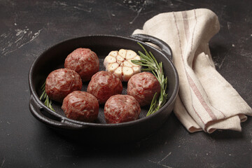 Raw meatballs seasoned with rosemary and garlic are waiting to be cooked in a cast iron pan top...