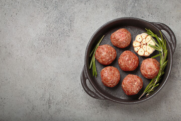 Raw meatballs seasoned with garlic and rosemary ready to be cooked in a cast iron pan, on gray...